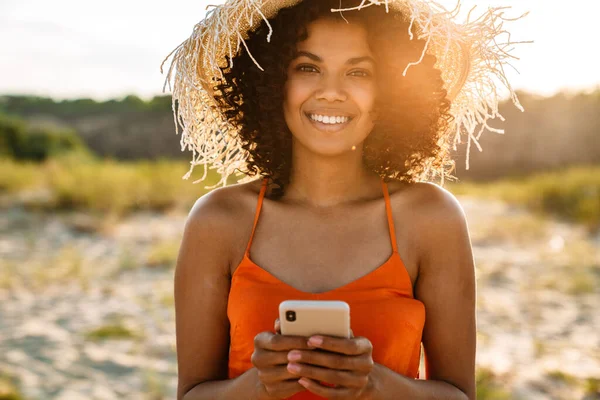 Sahilde cep telefonu kullanan güzel, gülümseyen bir Afrikalı kadın.
