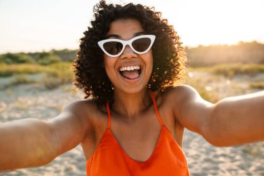 Güzel, mutlu, Afrikalı bir kadının dışarıda sahilde selfie çekerken görüntüsü.