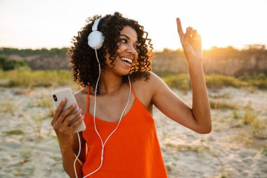 Sahilde kulaklıkla müzik dinlerken cep telefonu kullanan oldukça olumlu bir Afrikalı kadının görüntüsü