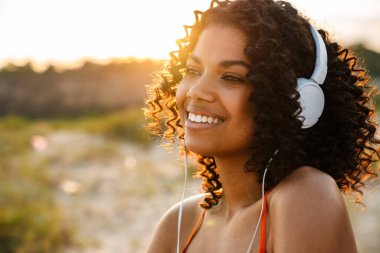 Sahilde kulaklıkla müzik dinleyen Afrikalı güzel bir kadının görüntüsü.