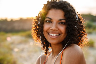 Sahilde kulaklıkla müzik dinleyen Afrikalı güzel bir kadının görüntüsü.