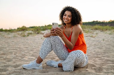 Kumsalda cep telefonu kullanan mutlu genç bir kadın.