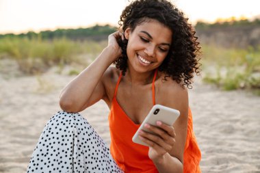 Kumsalda cep telefonu kullanan mutlu genç bir kadın.