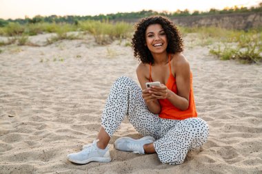 Dışarıdaki sahilde akıllı telefon kullanan oldukça olumlu bir Afrikalı kadının görüntüsü.