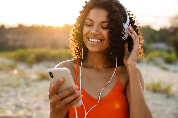 Mujer Africana Joven Feliz Escuchando Música Con Auriculares Playa Sosteniendo —  Fotos de Stock