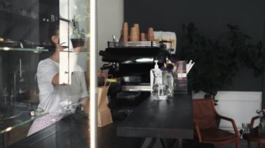 Maske takan genç ve güzel bir kadın kafeden bir şey alıyor ve karantina sırasında akıllı telefonla ödeme yapıyor.