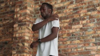 Yakışıklı Afro-Amerikan bir adam ısınma egzersizleri yapıyor. Omuzlarını içeride hareket ettiriyor.