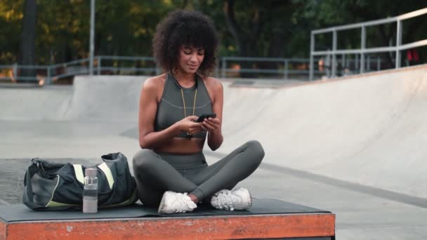 公園で屋外携帯電話を使用して若い楽観的なフィットネス女性 — ストック動画