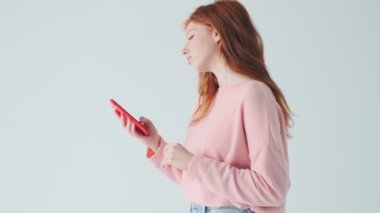 Beyaz duvar arkasında izole edilmiş cep telefonu kullanan genç kızıl saçlı güzel kız.