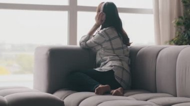 Genç hamile esmer kadın evde kulaklıkla müzik dinliyor.