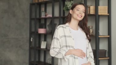 Genç, hamile, iyimser bir kadın evde yürüyor.