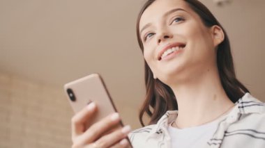 Evde cep telefonu kullanan mutlu hamile esmer kadın.