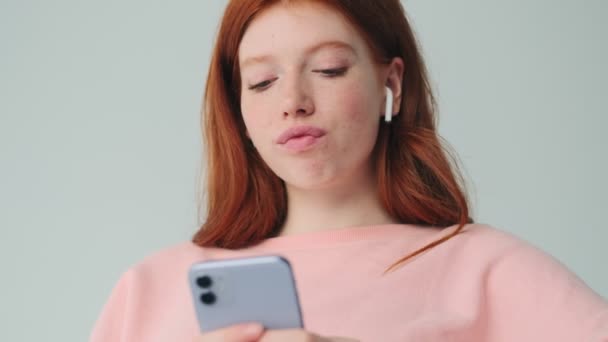 Positivo Rossa Ragazza Utilizzando Telefono Cellulare Auricolari Isolati Sfondo Bianco — Video Stock