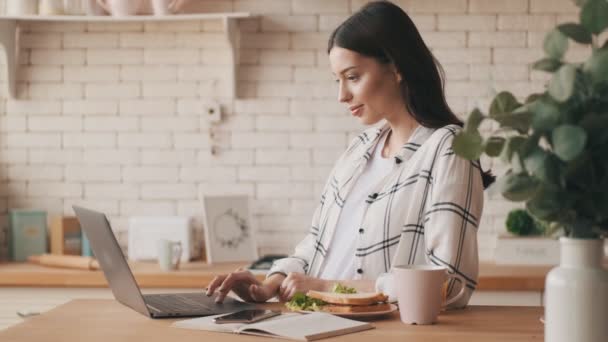 Mujer Morena Optimista Usando Computadora Portátil Cocina Mientras Desayuna Casa — Vídeo de stock