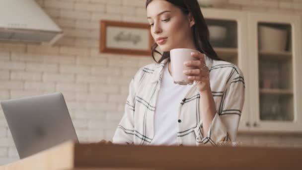 集中的孕妇在家里的厨房里使用笔记本电脑 喝咖啡 — 图库视频影像