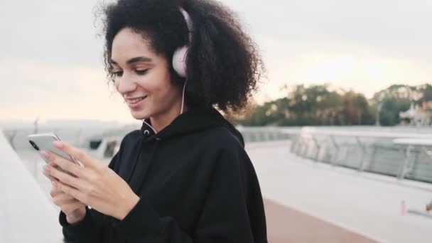 Przystojna Młoda Amerykanka Słuchawkami Korzysta Smartfona Spacerując Moście Miejskim — Wideo stockowe