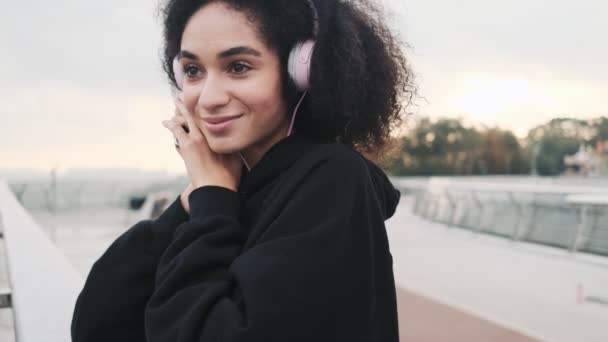 Potěšená Mladá Američanka Sluchátky Poslouchá Hudbu Při Chůzi Městském Mostě — Stock video