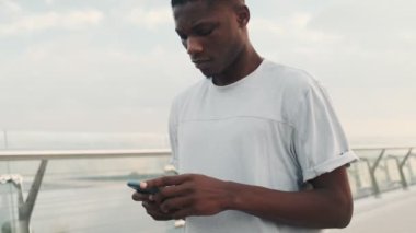 Yoğunlaşmış bir Afrikalı Amerikalı, şehir köprüsünde yürürken akıllı telefonunu kullanıyor.