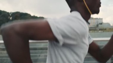 Kulaklıklı Afro-Amerikan bir adamın yan görüntüsü köprünün dışında koşuyor.