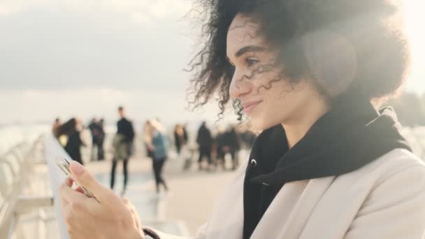 幸せなアメリカ人女性が街の橋の外を歩いている間にスマートフォンを使っています — ストック動画
