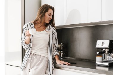 Genç, güzel, beyaz bir kadın. Gülümsüyor ve evde kahve içiyor.