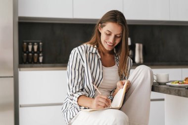 Evde kahvaltı ederken deftere yazı yazan güzel beyaz bir kadın.