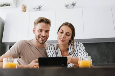 Evde kahvaltı yaparken cep telefonuna bakan beyaz bir çift.