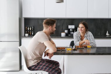 Genç, güzel, beyaz bir çift evde kahvaltı ederken masada oturuyor.