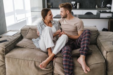 Evdeki kanepede otururken gülümseyen ve sarılan güzel beyaz bir çift.