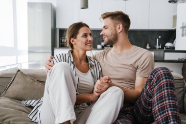 Evdeki kanepede otururken gülümseyen ve sarılan güzel beyaz bir çift.