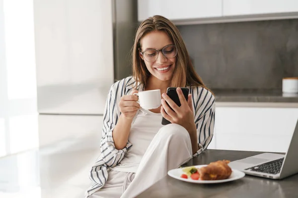 Fiatal Gyönyörű Kaukázusi Kezében Mobiltelefon Miközben Otthon Reggelizik — Stock Fotó