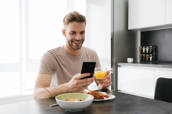 Ung Stilig Kaukasisk Man Håller Mobiltelefon Medan Äter Frukost Hemma — Stockfoto