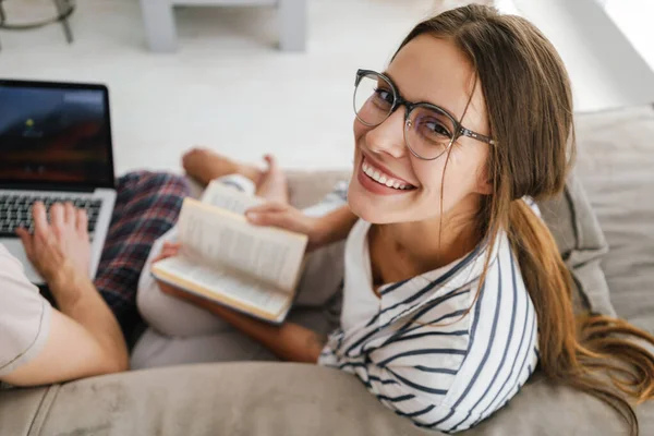 Junges Kaukasisches Paar Hält Laptop Und Liest Buch Während Hause — Stockfoto