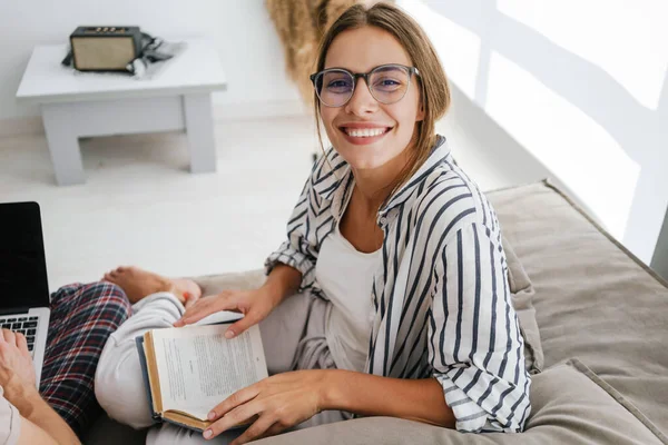 Joven Mujer Caucásica Sonriendo Leyendo Libro Mientras Está Sentado Sofá —  Fotos de Stock