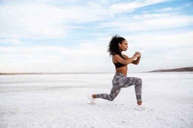 Kendine güvenen genç Afrikalı kadın tuz gölünde esneme egzersizleri yapıyor.