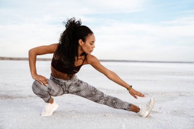 Atletik Afro-Amerikan sporcu kadının doğa üzerinde çalışırken egzersiz yapması.