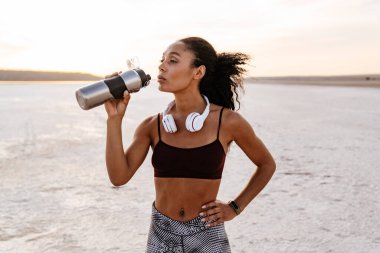 Genç Afro-Amerikan sporcu kadın görüntüsü. Doğa üzerinde çalışırken su içiyor.