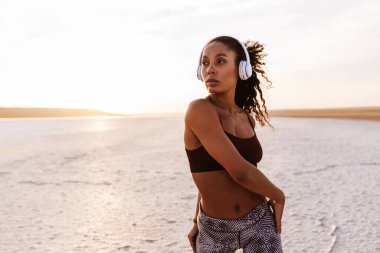 Afrika kökenli Amerikalı kulaklıklı bir kadının doğa üzerinde çalışırken egzersiz yapması.