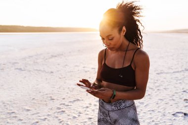 Afrika kökenli Amerikalı sporcunun doğa üzerinde çalışırken kulaklık ve cep telefonu kullanması.