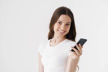 Beyaz arka planda izole edilmiş cep telefonu kullanan günlük giysiler giyen mutlu genç bir kadın.