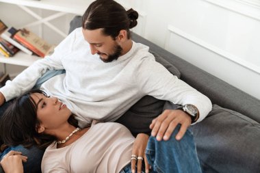 Romantik mutlu çiftin evdeki kanepede dinlenirken kucaklaşıp konuştuğu bir fotoğraf.