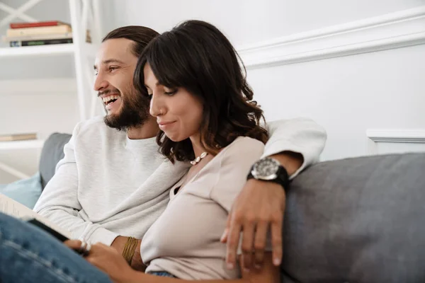 Imagen Pareja Caucásica Alegre Leyendo Libro Abrazándose Mientras Sienta Sofá — Foto de Stock