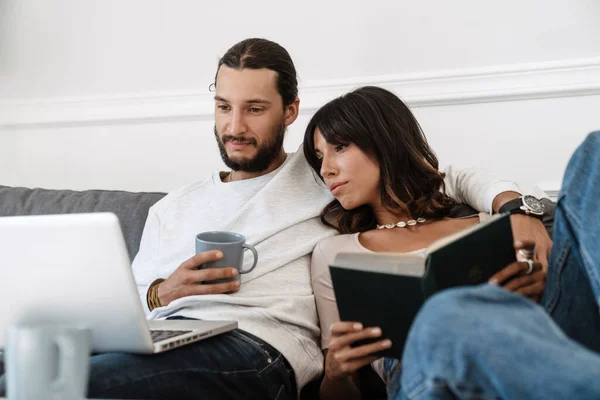 Imagen Pareja Hermosa Enfocada Leyendo Libro Usando Ordenador Portátil Mientras — Foto de Stock