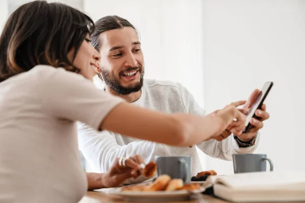 Obraz Uśmiechniętej Pięknej Pary Korzystającej Telefonu Komórkowego Podczas Śniadania Kuchni — Zdjęcie stockowe