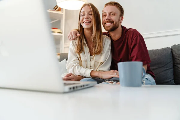 Imagen Jengibre Alegre Pareja Riendo Utilizando Ordenador Portátil Mientras Está —  Fotos de Stock