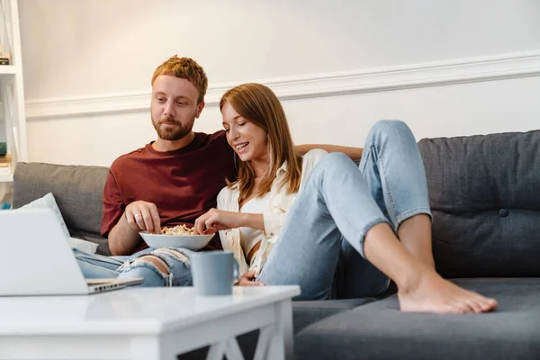 Imagen Jengibre Alegre Pareja Comiendo Palomitas Maíz Mientras Película Ordenador —  Fotos de Stock