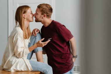 Evde cep telefonu kullanan ve öpüşen kızıl mutlu bir çift.