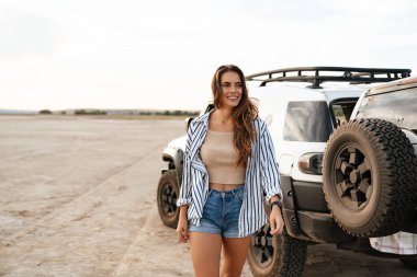 Çekici bir genç kadın arka planda arabasıyla plajda yürüyor.