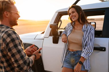 Birbirleriyle kaynaşırken ve arabalarına yaslanırken gülümseyen güzel bir çift.