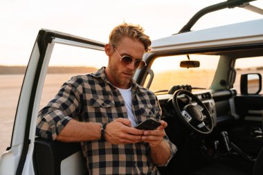 Kumsalın kapısında durup mesajlaşırken cep telefonu kullanan yakışıklı bir genç.